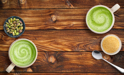 Pair of two matcha lattes and nuts with a spoon on a rich wood table top