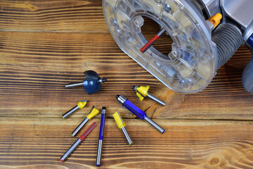 Wood router base and various shape cutter bit on wood board background. Carbide wood router cutter for wood profiling.