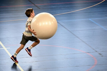 Énergie Sportive, jeune handballeur dribblant avec une grosse balle en plein élan - obrazy, fototapety, plakaty