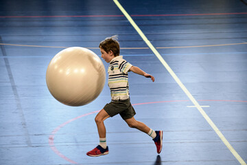 Énergie Sportive, jeune handballeur dribblant avec une grosse balle en plein élan - obrazy, fototapety, plakaty