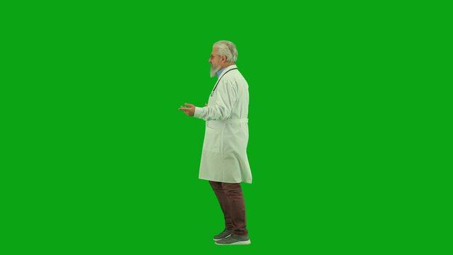 Portrait of aged man medic on chroma key green screen. Side view senior doctor walking through clinic or hospital and talking.