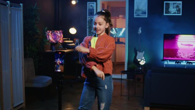 Zoom out shot on charismatic girl taking part in trends by sharing content of her performing viral choreography on popular hit song. Young online star films trending dance moves with tripod camera