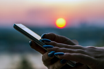 Close up view of female hands using smartphone near the river during sunset