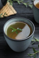 Cup of aromatic eucalyptus tea on black wooden table, closeup
