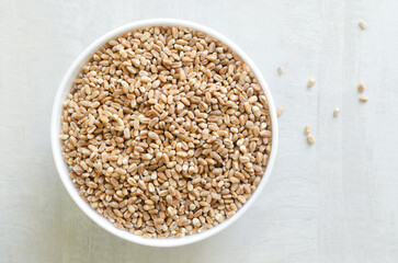 Wheat groats in a white bowl on a light background. Rustic style. Concept of healthy food. Horizontal orientation. Top view. Copy space