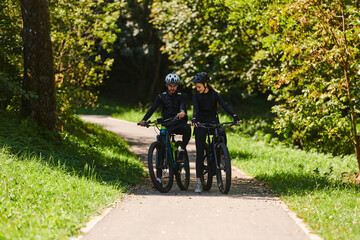 Naklejka premium A blissful couple, adorned in professional cycling gear, enjoys a romantic bicycle ride through a park, surrounded by modern natural attractions, radiating love and happiness