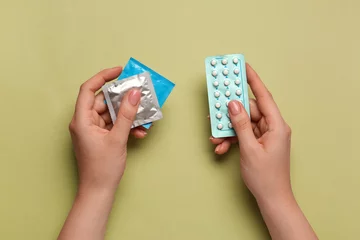 Fototapeten Woman with condoms and contraceptive pills on olive background, top view. Choosing birth control method © New Africa
