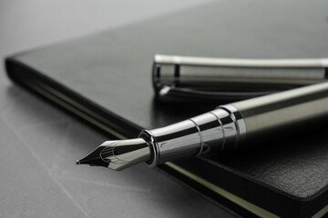 Stylish fountain pen, cap and leather notebook on light grey textured table, closeup