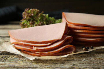 Slices of delicious boiled sausage with lettuce and spices on wooden table, closeup