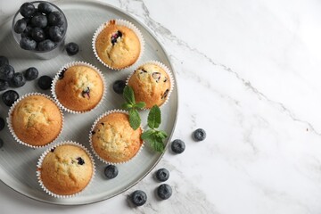 Delicious sweet muffins with blueberries and mint on white marble table, flat lay. Space for text