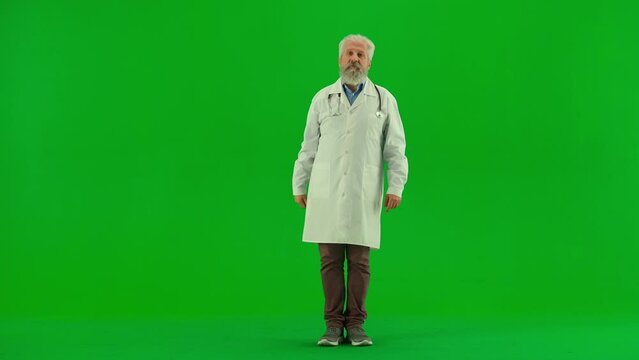 Portrait of aged man medic on chroma key green screen. Senior doctor in white coat standing showing pointing at empty area advertises clinic.