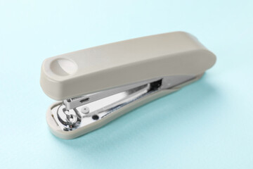 Beige stapler on light blue background, closeup