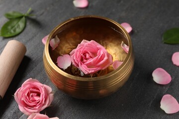 Tibetan singing bowl with water, beautiful rose flowers and mallet on gray table, closeup