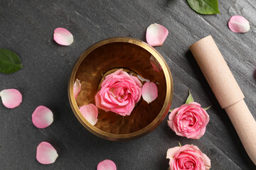 Tibetan singing bowl with water, beautiful rose flowers and mallet on gray table, flat lay