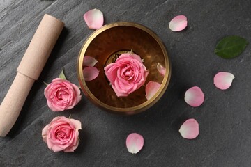 Tibetan singing bowl with water, beautiful rose flowers and mallet on gray table, flat lay