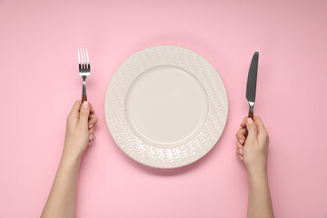 Woman holding fork and knife near empty plate at pink table, top view