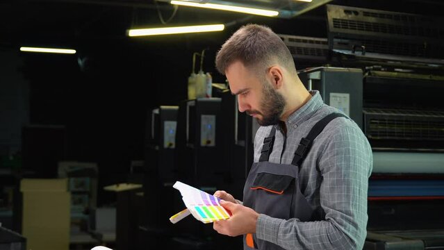 Worker in a printing and press center uses a color palette to select the correct shade of color from CMYK printed sheet