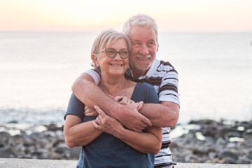 couple of seniors hogging at the beach with a lot of love - retired together - woman with glasses...