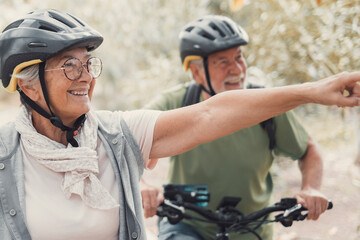 Two happy old mature people enjoying and riding bikes together to be fit and healthy outdoors. Active seniors having fun training in nature. Portrait of one old man smiling in a bike trip 