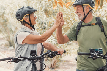 Couple of two seniors giving five together outdoors having fun with bicycles enjoying nature....