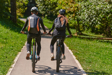 Naklejka premium A blissful couple, adorned in professional cycling gear, enjoys a romantic bicycle ride through a park, surrounded by modern natural attractions, radiating love and happiness