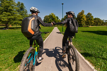 A sweet couple, adorned in cycling gear, rides their bicycles, their hands interlocked in a romantic embrace, capturing the essence of love, adventure, and joy on a sunlit path