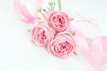 Three pink roses with ribbon and giftbox on the white table