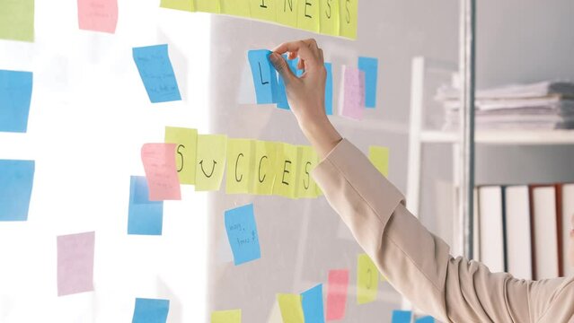 Young smiley attractive businesswoman using sticky notes in glass wall to writing strategy business plan to development grow to success