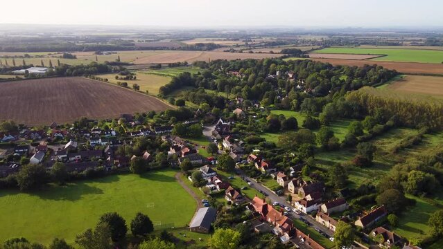 Slowly flying over a small village in England. Trees surround the homes with fields stretching to the horizon 