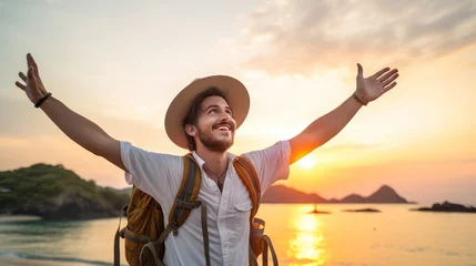Foto op Plexiglas A Happy male traveler in hat and backpack raising arms on beach at sunset Delightful male traveler enjoying quiet time, travel and mental health. © Phoophinyo