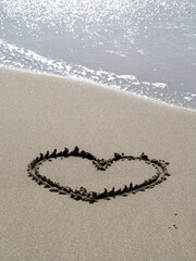 砂浜の波打ち際に描かれたハート。(縦構図)
