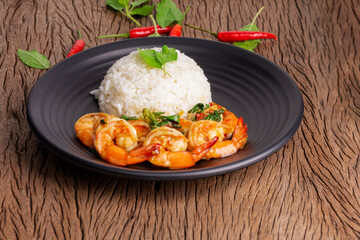 Stir-fried shrimp with basil Thai street food, arranged on a black plate, spicy Thai food, placed on a wooden table. Close-up top view.