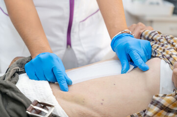hand of Doctor is using clean cotton dressing infection wound at a man abdomen. Bandage for wound...