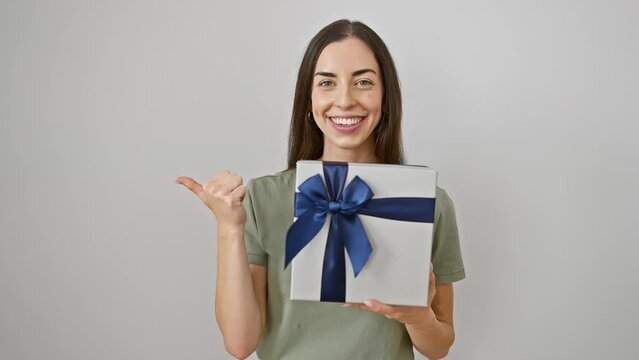 Joyful young hispanic woman confidently showing off her birthday present, thumb pointing good vibes to the side, isolated on a white cutout background.