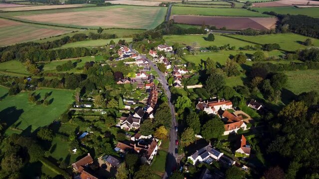 Aeiral footage of a village in the middle of the English Countryside. Plowed and fallow fields surround the homes. 