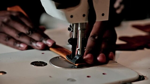 Black hands operate a sewing machine to sew together a leather strap