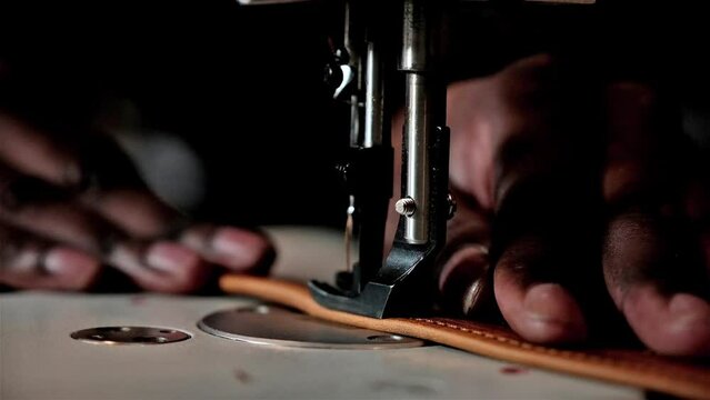 Black man using a sewing machine to sew leather straps