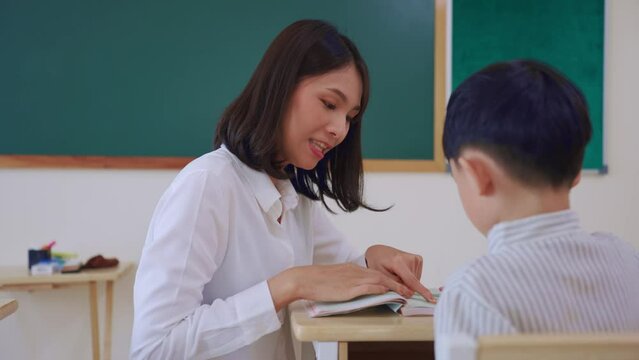 Asian beautiful female teacher teaching young boy student in classroom. 