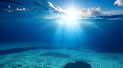 Poster Sunlight shining through the surface of the blue ocean, sea, with dark waters and sandy seabed below. © Mariana