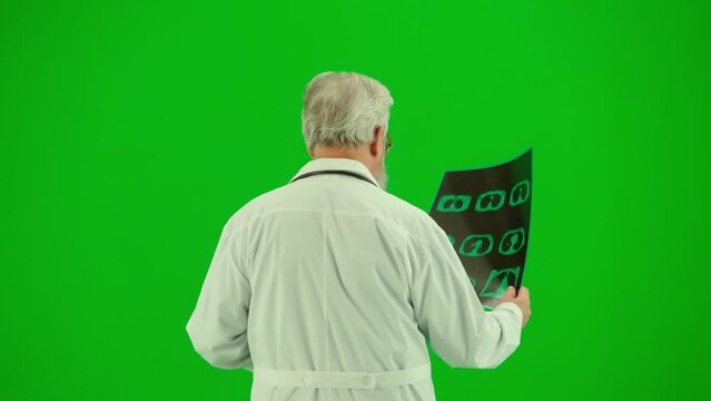 Portrait of man medic on chroma key green screen. Close up back view senior doctor in uniform walking holding x-ray looking at it.