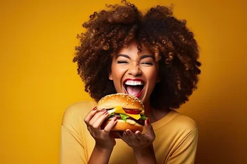 Foto op Plexiglas woman eating a hamburger. Person eating a sandwich. black woman eat burger on yellow background © KirKam