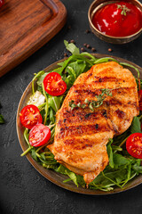 Grilled chicken breast with arugula and tomatoes on a plate and black table vertical photo