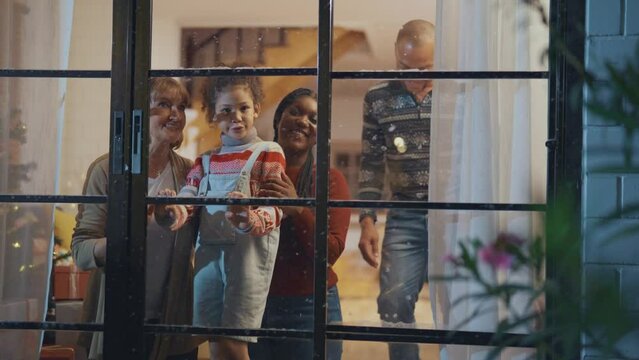 Adorable child looking at the window and first snow flakes with family.