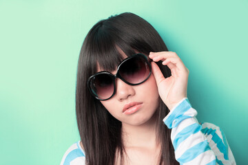 Fototapeta premium Cool Asian woman leaning against a wall with sunglasses.