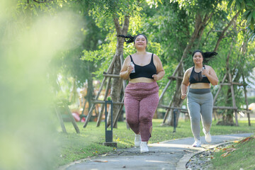 Cheerful two women overweight in sportswear have fun exercising in garden. Asian girls plus size wear sports uniform are friend together running exercise in green public park, healthy concept.