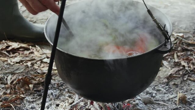 stirring fish soup with a ladle, cooking fish soup in a cauldron over a fire in nature