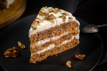 Carrot cake with butter cream and walnuts on a dark background