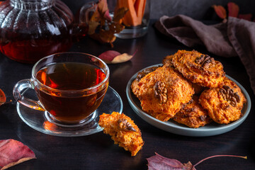 Carrot cookies with walnuts and tea in a cup against a dark background