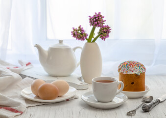 Fototapeta na wymiar Easter still life with painted eggs, Easter cake and tea in a cup on the windowsill on a sunny day