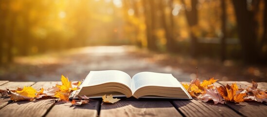 Book open outdoors on wooden table with autumn leaves falling.